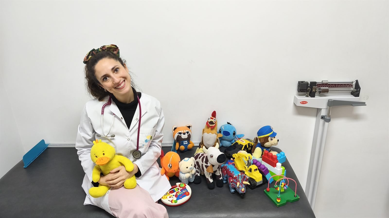 Pediatra de Pediatras Junt@s sentada en la camilla del consultorio junto a peluches y juguetes